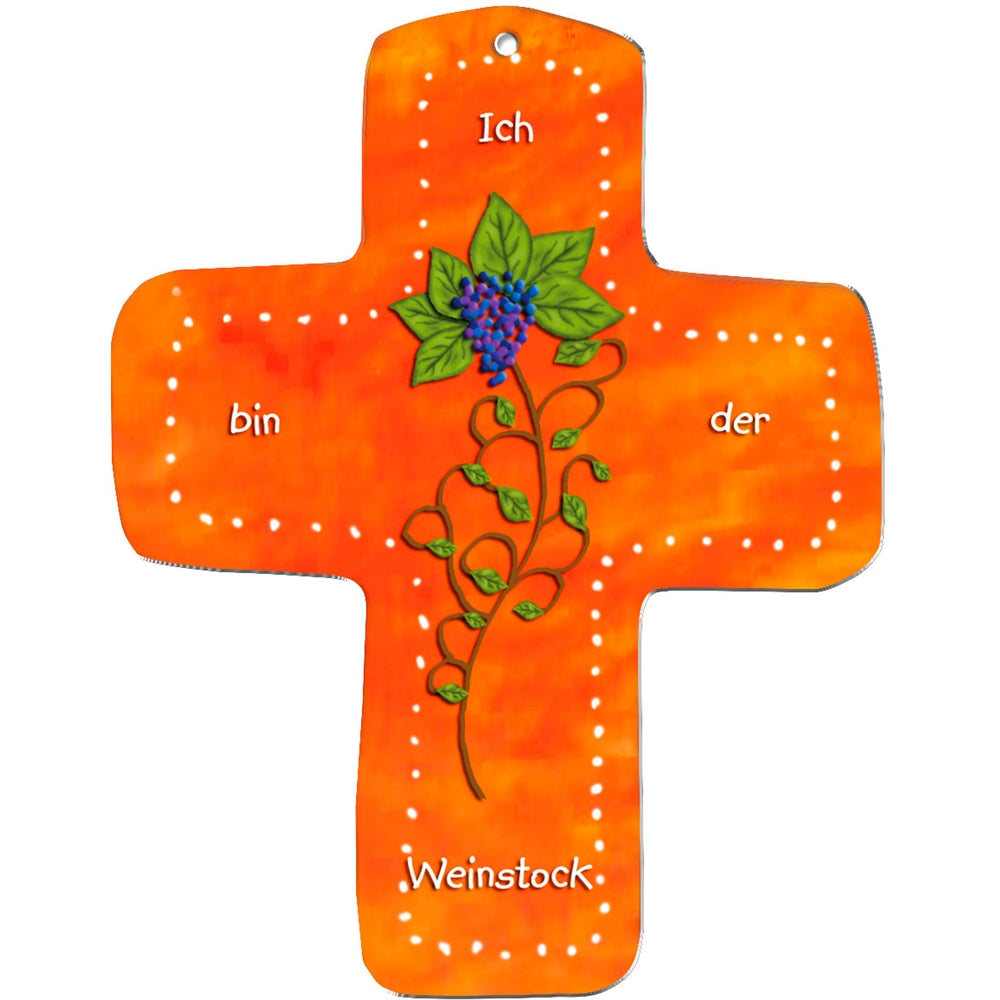 Das metALUm Wandkreuz aus orangefarbenem MDF hat einen gepunkteten weißen Rand, eine gemalte Weinrebe mit grünen Blättern und lila Trauben und den Text "Ich bin der Weinstock". Dank des Lochs an der Spitze eignet es sich perfekt als Geschenk für Kinder.