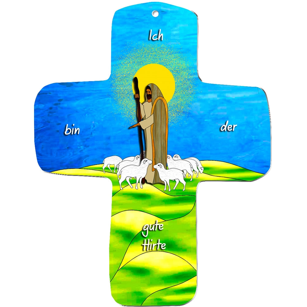 Ein farbenfrohes metALUm Wandkreuz zeigt Jesus in einem braunen Gewand mit einem Hirtenstab, sechs weißen Schafen auf grünen Hügeln, einem gelben Heiligenschein und einem blauen Himmel. Der deutsche Text lautet: "Ich bin der gute Hirte" - ein ideales Geschenk für Kinder.